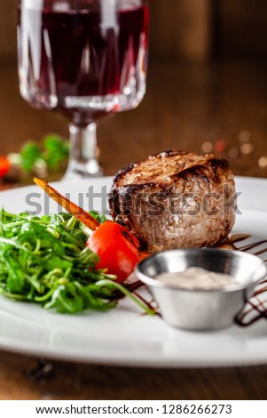 Georgian cuisine. Juicy beef steak, veal steak on a white plate with roasted rocket, grilled vegetables and sauce. On the table is a glass of red pomegranate wine. Serving dishes in the restaurant