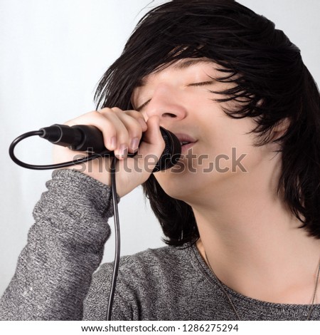Black hair young guy in emo style is singing in microphone on white background.