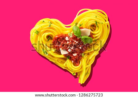 Decorative heart-shaped Italian pasta portion, formed of cooked spaghetti, topped with tomatoes, basil, and parmesan cheese, viewed in close-up, from above on pink background. Love for food concept Royalty-Free Stock Photo #1286275723