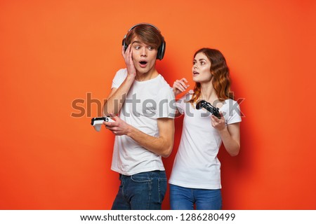 Emotional young people with joysticks in their hands on an orange background are standing next to each other              