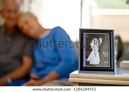 Happy senior couple sitting behind a framed photo of a young couple on their wedding day.