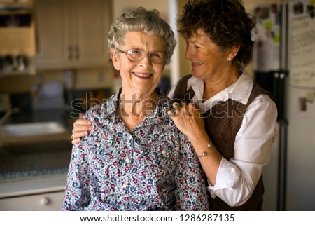 Smiling mature woman gives her elderly mother an affectionate squeeze.