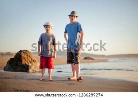 Portrait of two brothers standing side by side on a sandy beach.