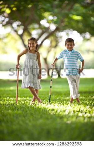 Brother and sister posing for a photo leaning on croquet mallets.