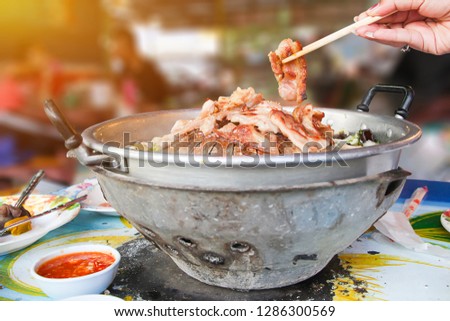 Hand hold chopsticks with Thai barbecue Grill Pork on hot pan buffet, vegetable and soup on hot pan, Moo Kra Ta (thai word) - Image Royalty-Free Stock Photo #1286300569