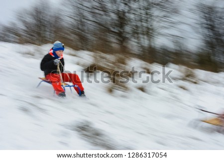 the boy descends from the hills in the sled, the movement is blurred