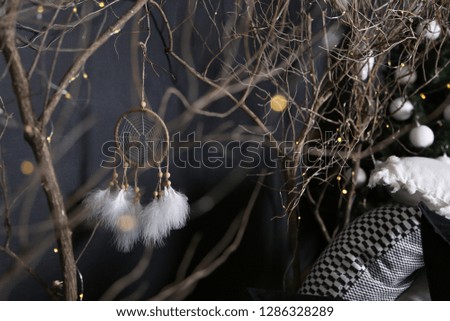 Dreamcatcher and branch trees against the background of a green fir-tree with white spheres and pieces of multi-colored pillows.