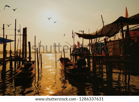 Beautiful scenery of sea landscape, traditional fishing boats moored at seaside with bamboo pier and birds are flying in sunrise sky background at morning time, back lighting photography 