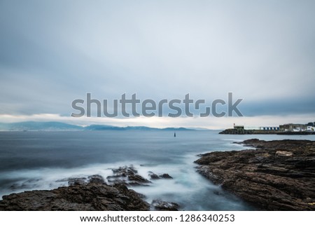 Cliffs and small lighthouse on a cloudy Winter day in Portonovo in Galicia, Spain, with the entrance to the Ria de Pontevedra in the background. Long exposure.