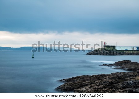Cliffs and small lighthouse on a cloudy Winter day in Portonovo in Galicia, Spain, with the entrance to the Ria de Pontevedra in the background. Long exposure.