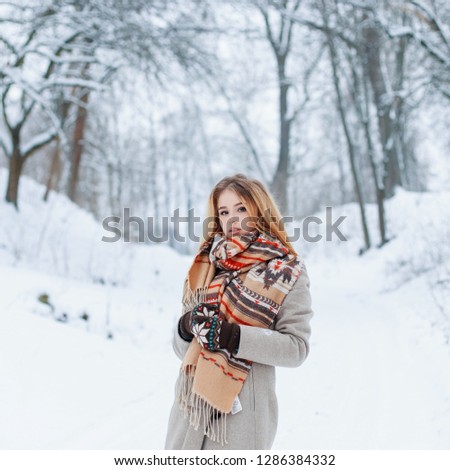 Attractive young girl stylish with a woolen warm scarf in a trendy gray winter coat in vintage knitted mittens spends the weekend in the park. Charming stylish girl.