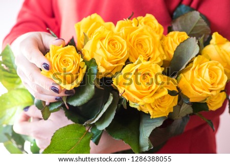 A woman in a red dress holds a large bouquet of flowers. Fresh yellow roses