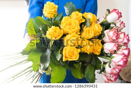 A bouquet of fresh pink and yellow flowers. Woman in a blue dress holds flowers