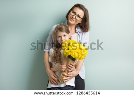 Portrait of mother and child daughter together embracing smiling with bouquet of yellow spring flowers. Mothers day, spring family holiday concept, pastel green mint wall background