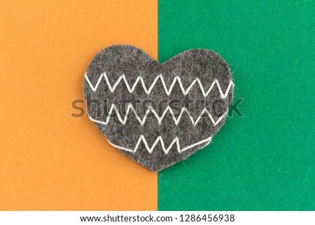 Valentines day background with beautiful handmade heart lying on cardboard split into two color parts.Love, romance concept Felt heart with geometric zig zag embroidered lines. Stylish chevron pattern