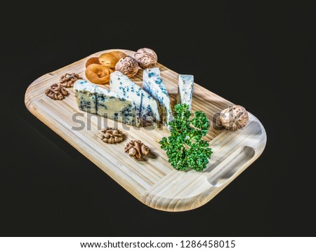 Some peaces of the cheese blue mold roquefort  with dried apricot and peaces of the nuts with parsley at the wooden desk and background