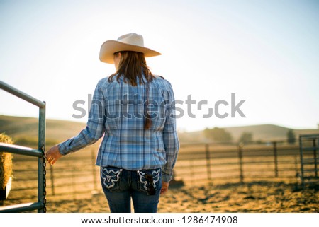 Farmer's wife wearing a cowboy hat opening a gate out on the ranch.