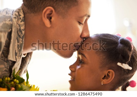 Soldier kissing his young daughter on the forehead.