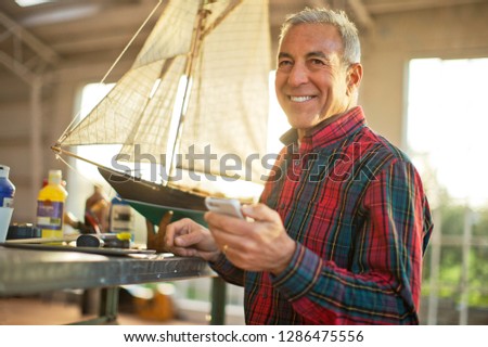 Portrait of a smiling senior man with a model boat inside his garage.