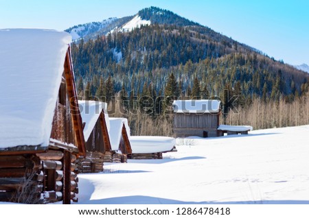 Row of snow-covered log cabins in a wintry setting.