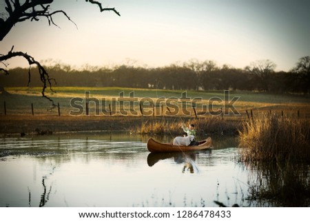 Young adult man fishing in a canoe with his dog on a lake.
