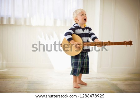 Toddler playing with a wooden banjo.