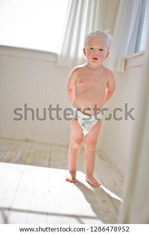 Shirtless young toddler standing barefoot in a room wearing nappies.
