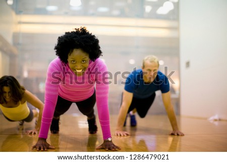 Portrait of a smiling young woman doing press ups inside a gym.