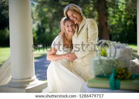 Young adult bride hugging her mature mother while outside.