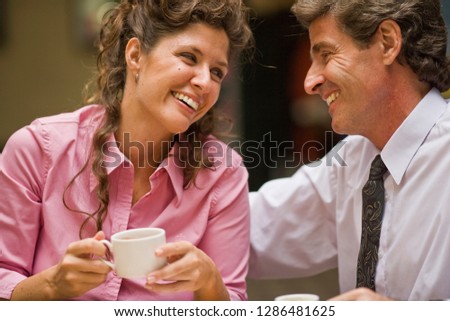 Happy mid-adult woman holding a coffee cup sitting with her husband at a cafe.