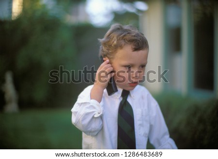 A formally dressed little boy speaking on a cell phone.