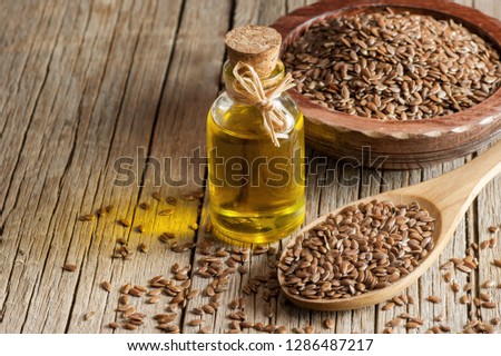 Heap of Flax seeds or linseeds in spoon and bowl with glass of linseed oil on wooden backdrop. Flaxseed or linseed concept. Flax seed dietary fiber Royalty-Free Stock Photo #1286487217