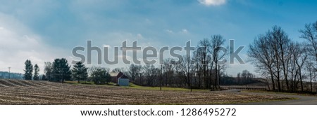 Rural countryside web banner. Harvested corn field in the foreground with a red barn and grain bin in the background with blue sky and clouds on a sunny winter day.