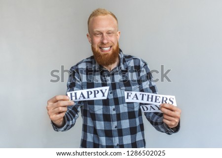 Red hair mature man standing isolated on grey wall holding happy fathers day congratualition letters looking camera smiling cheerful