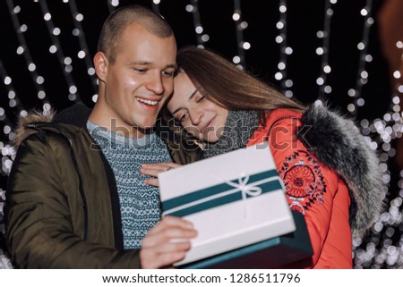 Young couple together opens box with a gift. The woman gives a man birthday present on winter evening. Romantic people with love. - Image