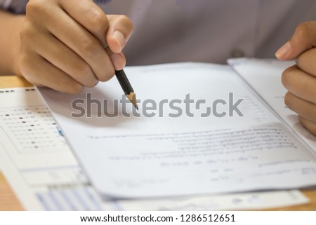 Education test concept : Man Hands high school, university student holding pencil for testing exams writing answer sheet and exercise for taking in exam paper on wood table at classroom with uniforma