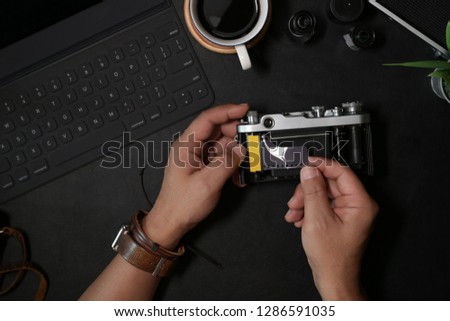 Man hand loading film 35mm on vintage camera at dark leather desk