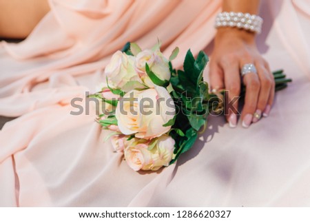 Bride's hand and wedding bouquet on the train of a dress ourdoors. Close up.