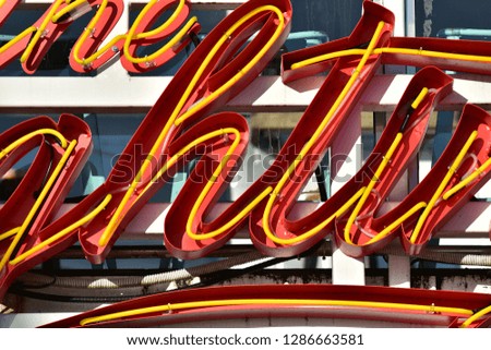 Detail of sign letters made of bright yellow neon tubes on red background.