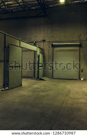 Empty back of industrial warehouse with concrete texture walls and floor and tall chainlink fence. 