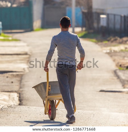 Worker carries a wheelbarrow at a construction site .