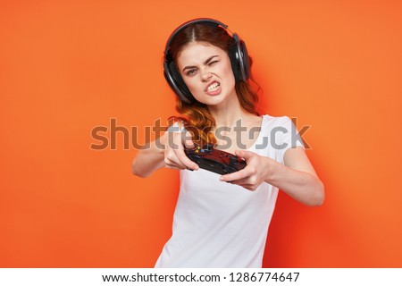 A gamer woman with a joystick and headphones bared teeth against an orange background                           