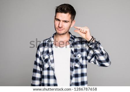 Beautiful man showing small thing while smiling and standing near white wall. Handsome man in a plaid shirt tells everyone about poor salary of his next door neighbor he hates so much.
