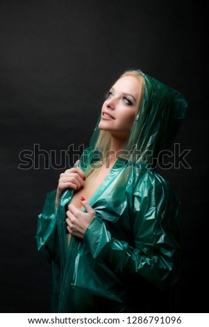Portrait of a young beautiful blond woman in a green raincoat looking up, a hood is put on her head. Shooting in a photo studio on a black background