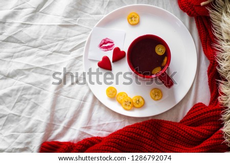 Red cup of tea with kumquat and two hearts cookies, a note with a kiss on a white bed. Valentines day concept   