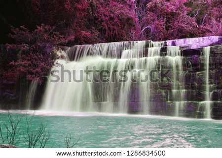 The beautiful waterfall in purple forrest down to emerald green lake. Striking nature.