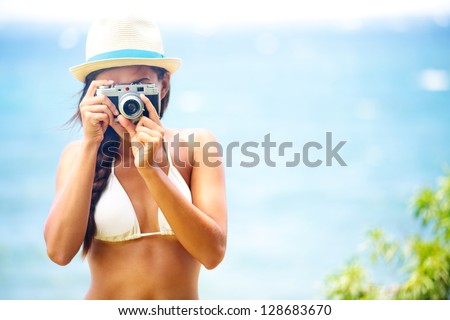 Summer beach woman holding vintage retro camera taking pictures looking at camera during summer holiday vacation travel at the ocean.