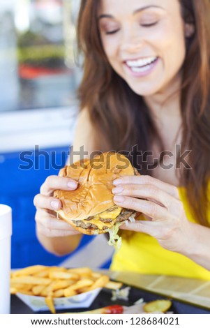 Cheerful young woman having delicious burger. Vertical Shot.
