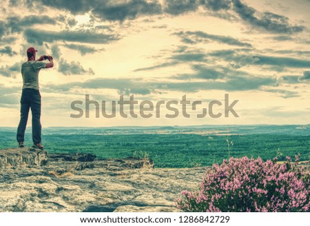 Tall young man on viewpoint holding his camera. Photographer taking picture of forest, sky and clouds on his vacation. Man travel alone