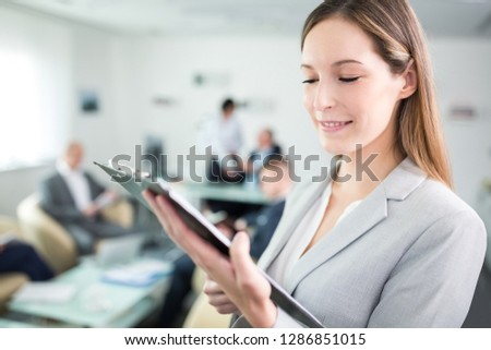Smiling businesswoman reading document on clipboard in meeting room at office